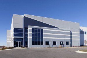 Gray industrial building with blue sky; glass windows, paved lot.