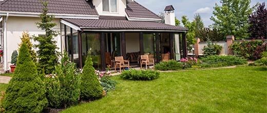 House with patio and lush green lawn, landscaped garden, and potted plants