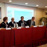 Un gruppo di persone è seduto a un lungo tavolo e sta tenendo una presentazione.