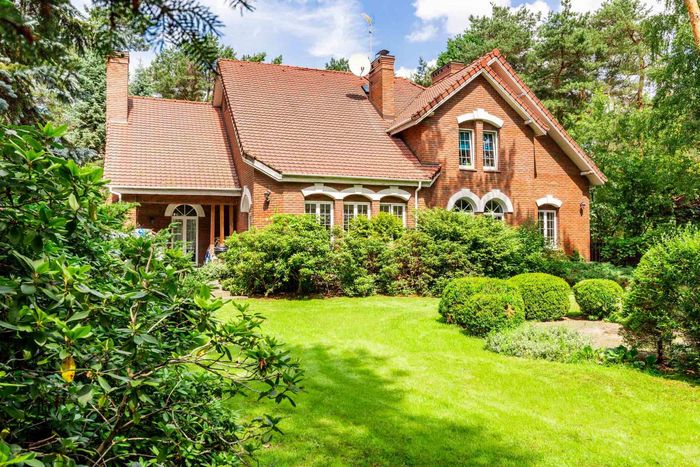 Brick house with red roof, green lawn, and lush surrounding trees.