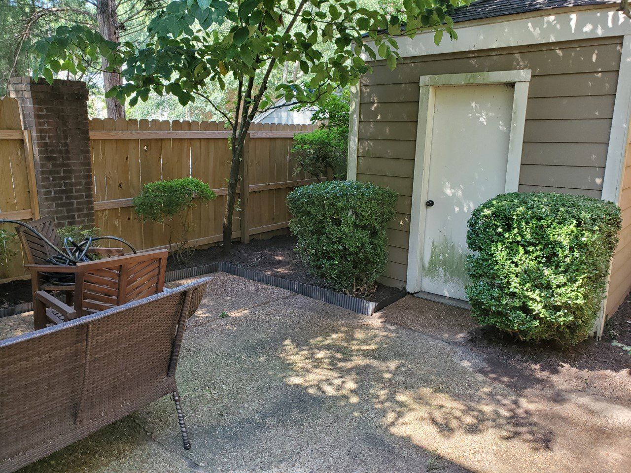 Patio with outdoor furniture, shed, wooden fence, and green bushes.