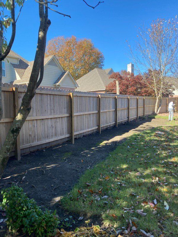 A wooden fence in a yard on a sunny day. Houses and trees are visible in the background.