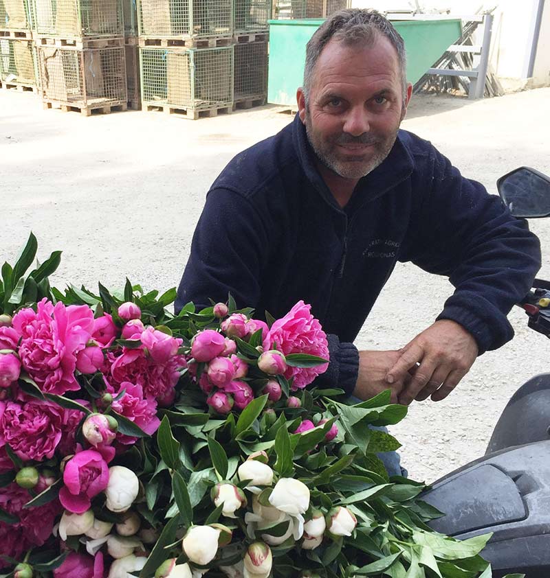 Producteur de pivoines devant des caisses de fleurs à la ferme