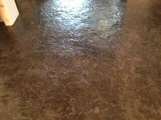 Dark, textured floor with swirled patterns and glossy areas, possibly stained concrete.