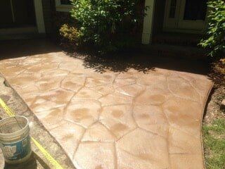 Stamped concrete walkway in brown tones with a bucket and greenery.