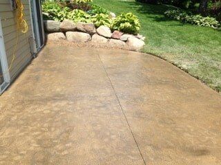 Brown concrete patio next to a green lawn, rock garden, and building.
