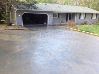 Gray house with open garage and wet asphalt driveway.