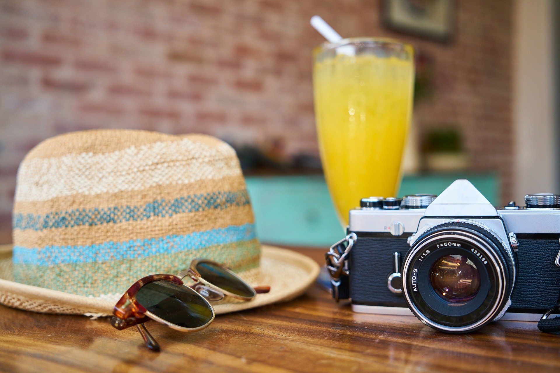 A hat sunglasses a camera and a glass of orange juice on a table