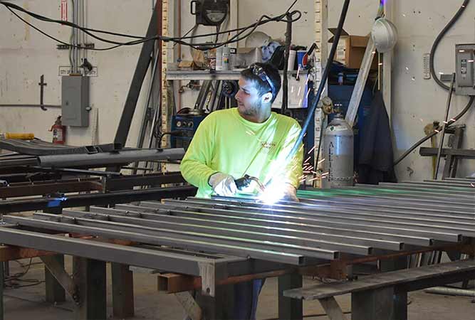 Welder in neon shirt welding metal bars in a workshop, sparks flying.