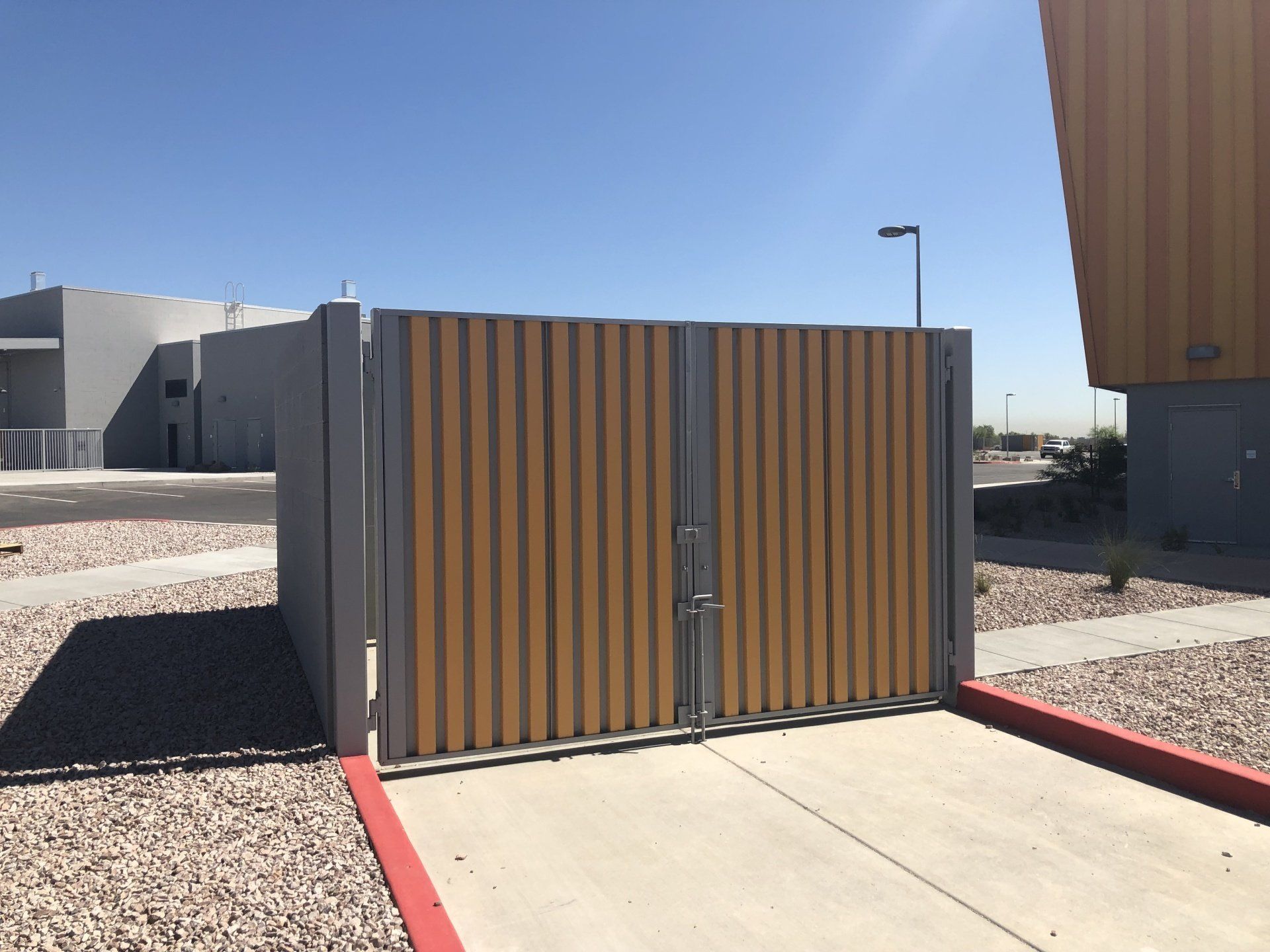 Metal and wood trash enclosure with a locked gate on a concrete pad.