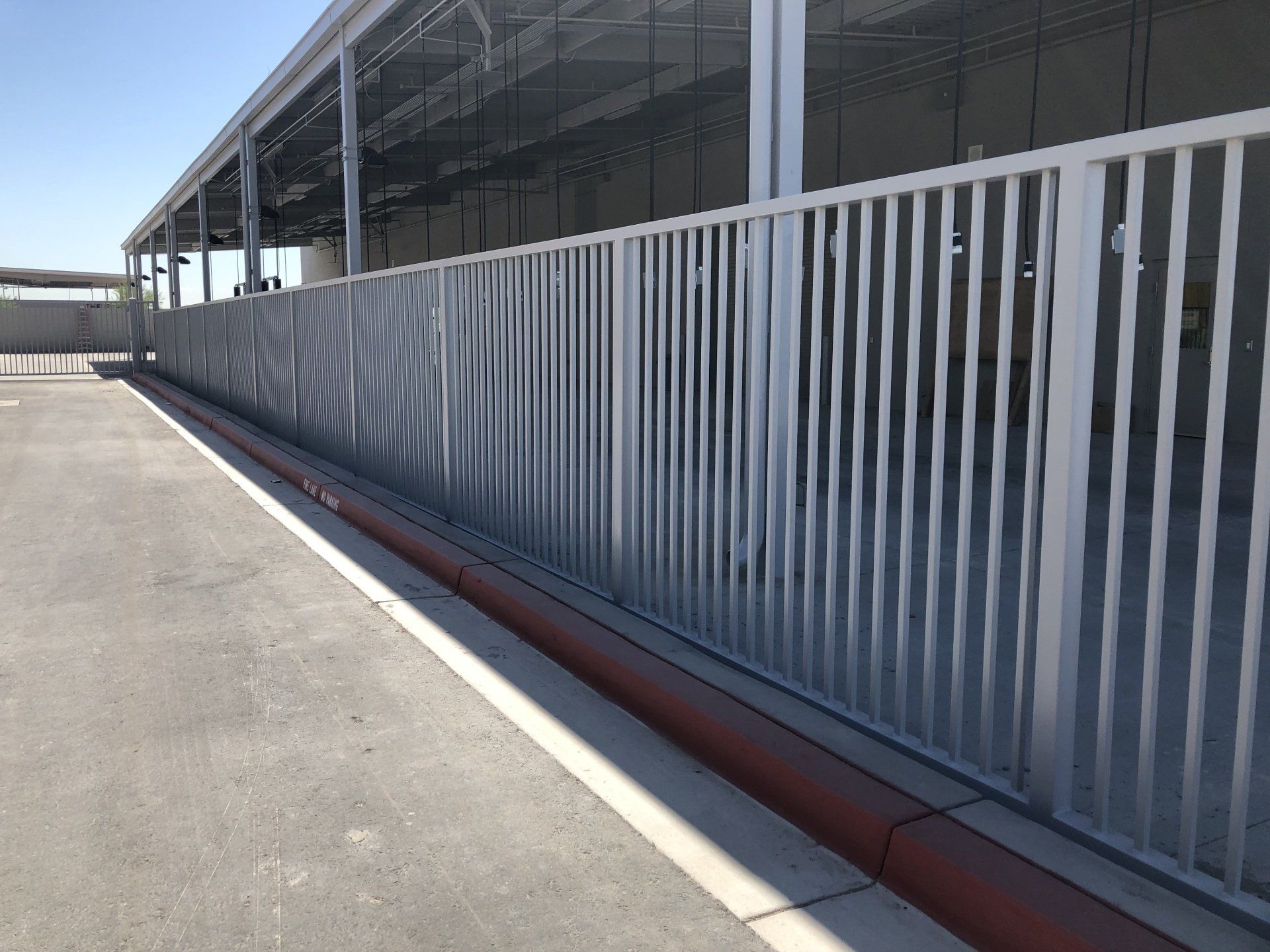 Metal fence with vertical bars along a building's side. Red curb runs along the base.