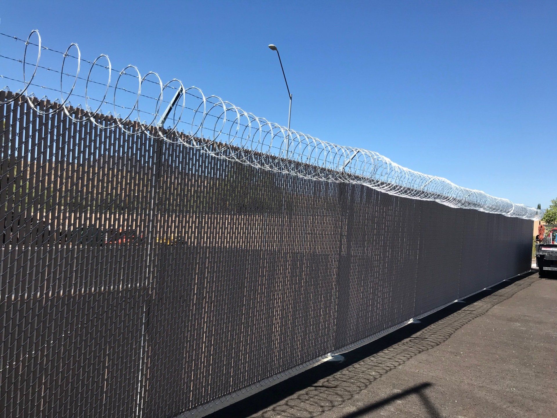 Black privacy fence with razor wire topping, on a sunny day.