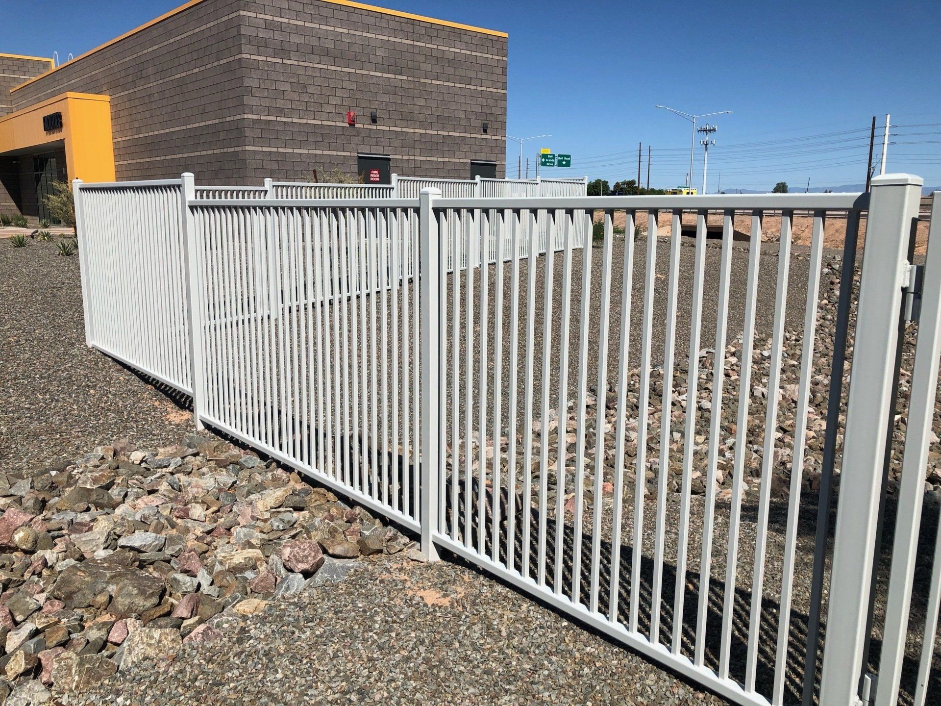 White metal fence in front of a brick building on a sunny day.