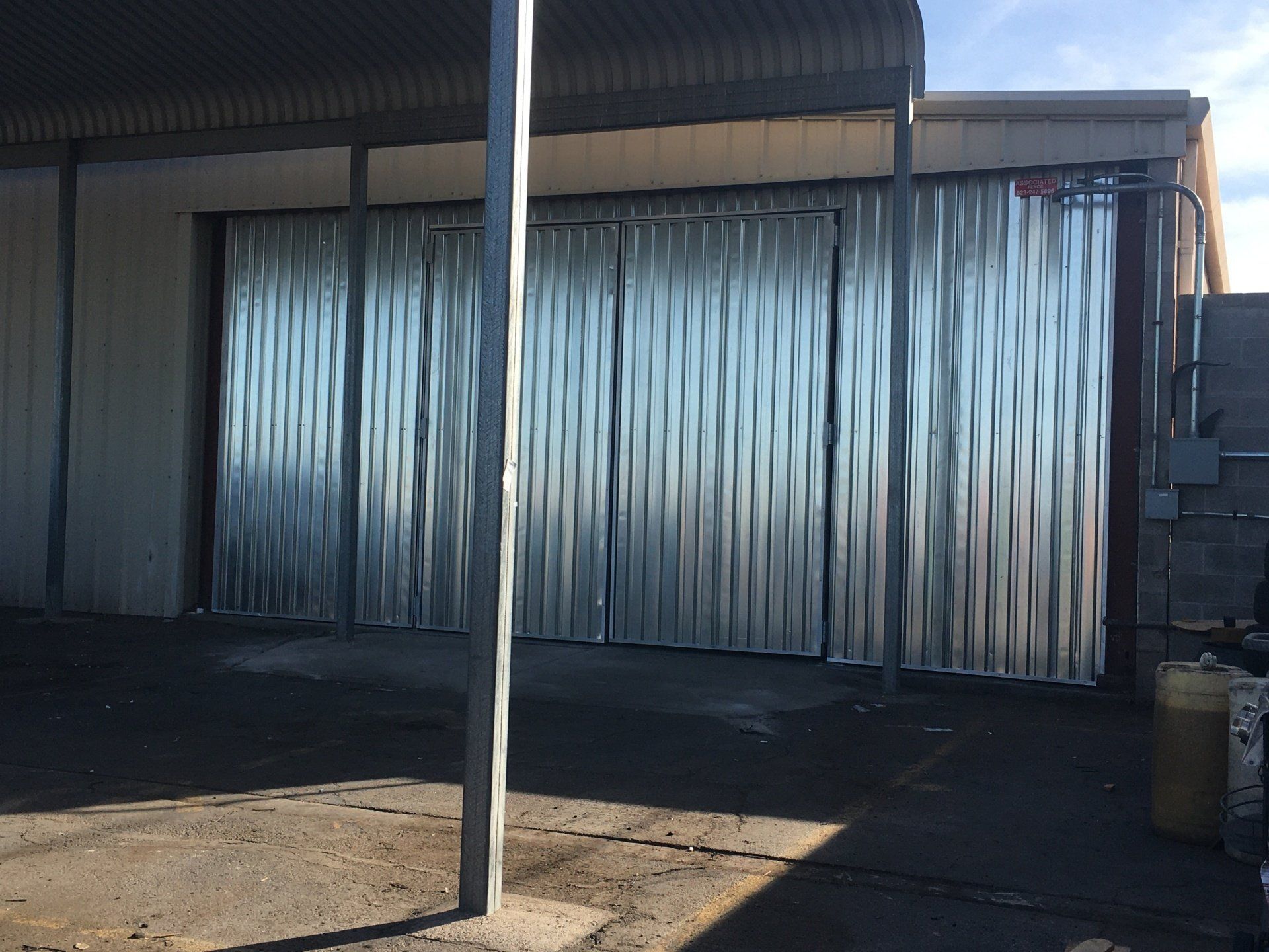Corrugated metal doors, closed, on a building. Gray metal, concrete ground, and a covered area.