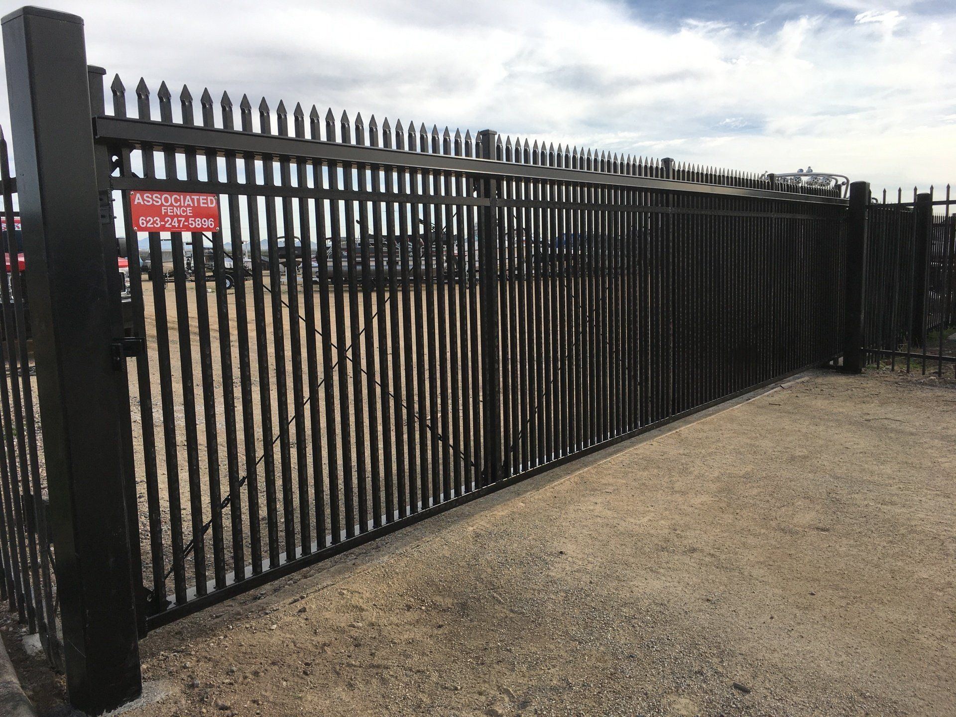 Black metal security fence in front of gravel, with a red sign visible.