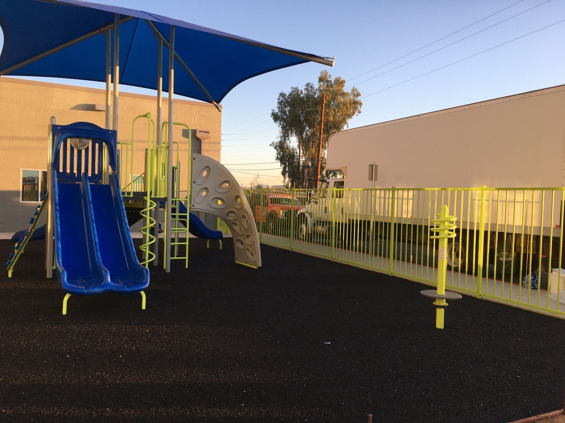 Playground with blue slides, climbing structure, and shaded area; black rubber surface.