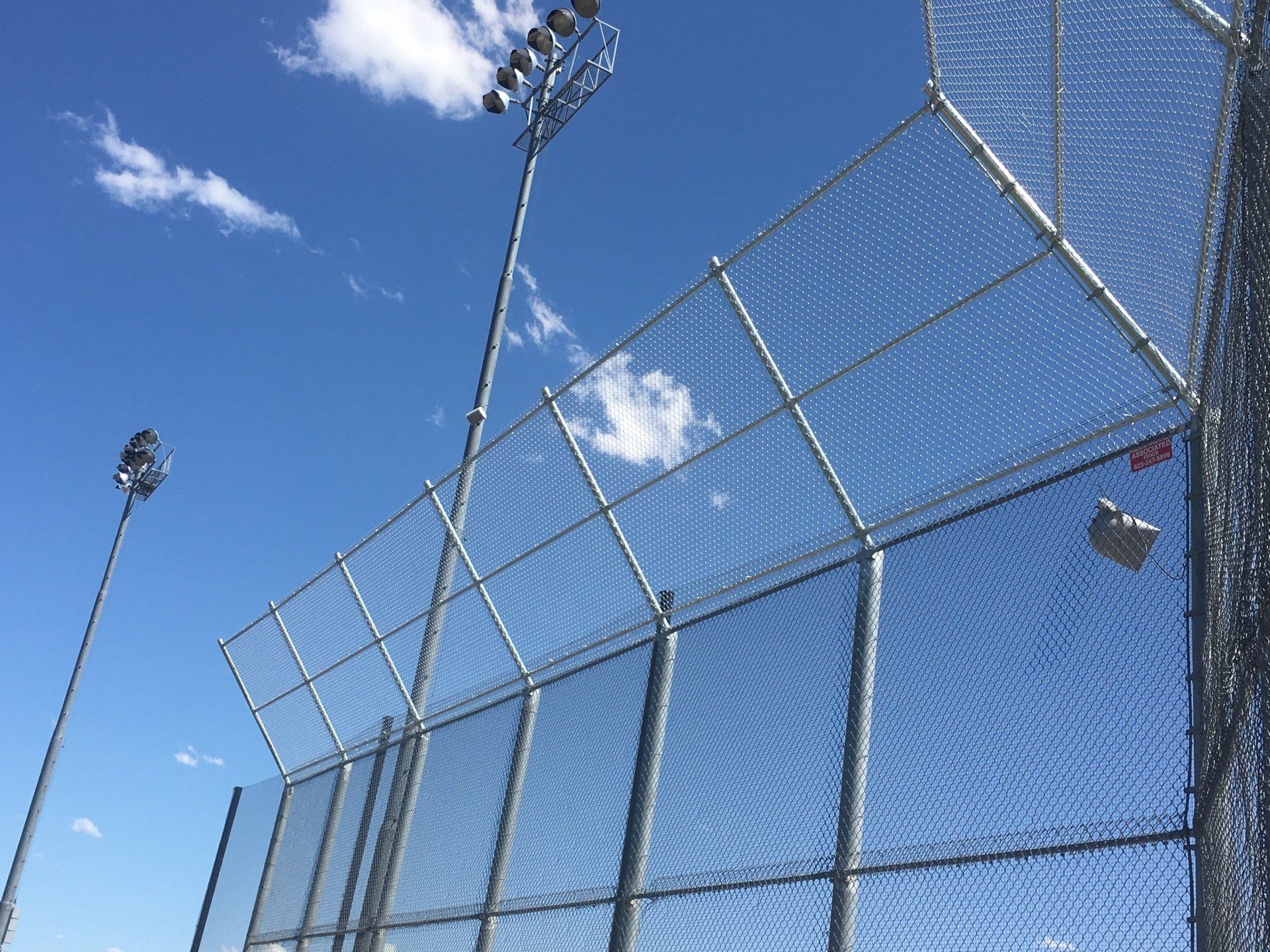 Chain-link fence under a bright blue sky with stadium lights.