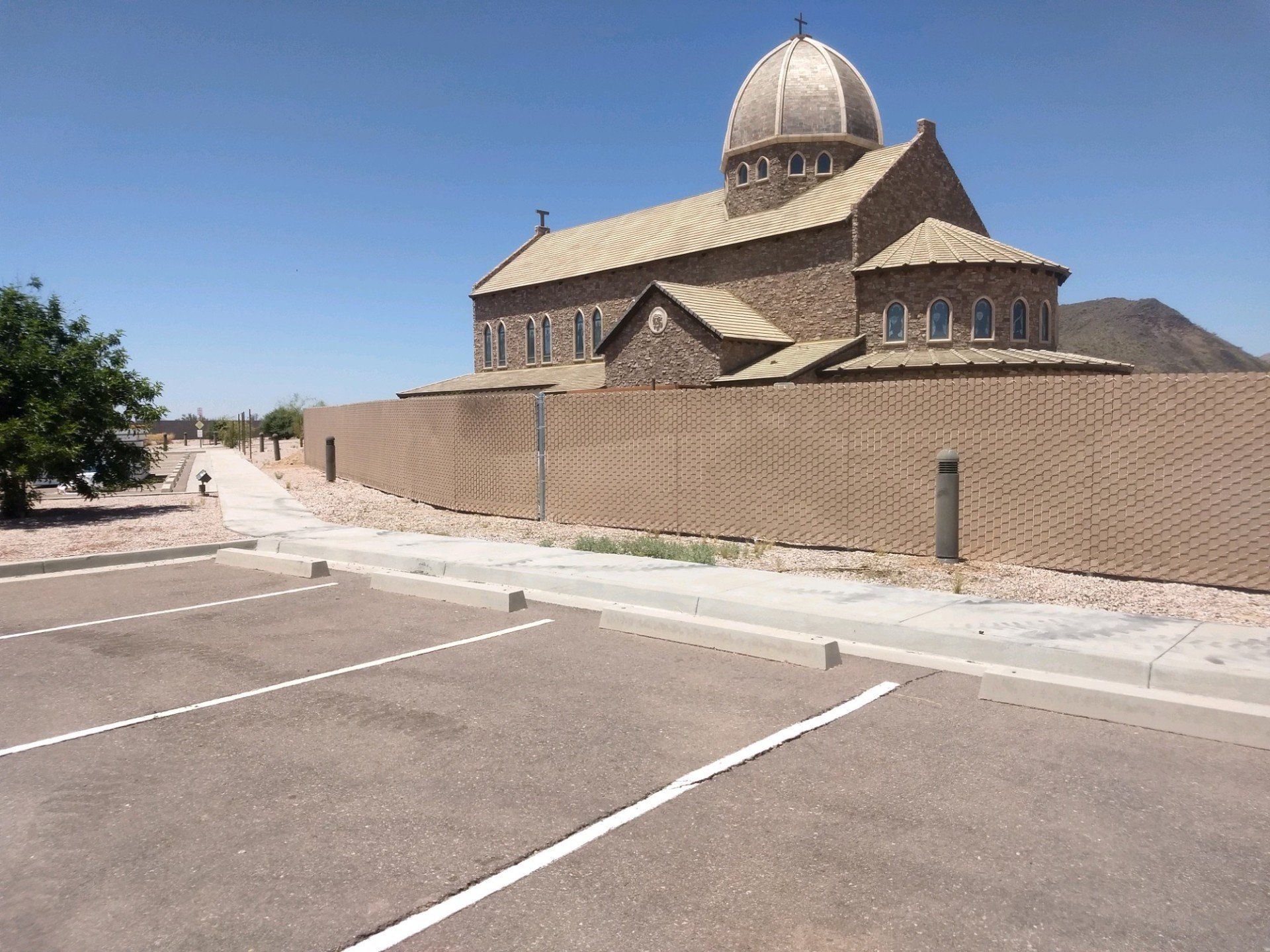 A large brick church with a dome behind a long brick wall and a parking lot.