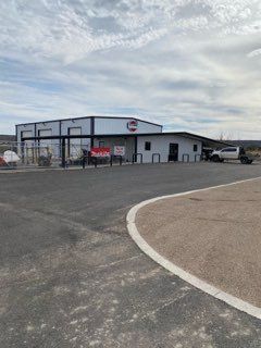 Small roadside storefront with glass front, white sign, and a mostly empty parking lot under cloudy sky