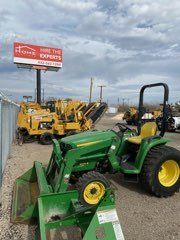 Green tractor with front loader in front of rows of yellow construction equipment at a dealer lot