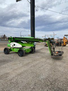 Green and white boom lift with extended arm in a gravel lot under cloudy sky