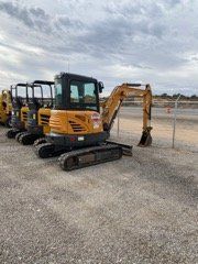 Yellow mini excavators lined up on a gravel lot under a cloudy sky