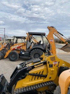 Yellow and black construction loaders and excavators parked on a gravel lot under cloudy sky