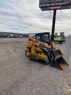 Yellow skid steer with bucket parked on gravel lot under cloudy sky