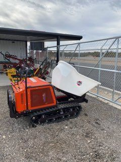 Orange tracked utility robot with white attachment beside a chain-link fence on gravel outdoors