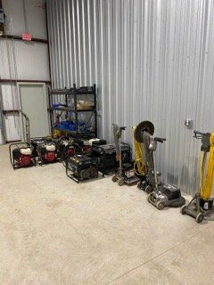 Small warehouse corner with power tools, generators, and yellow hand trucks against a corrugated metal wall.
