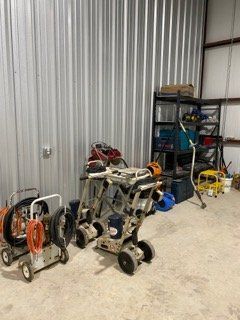 Workshop floor with two small wheeled machines and a metal storage shelf against a corrugated wall