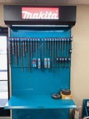 Makita tool display with hanging drill bits and accessories on a blue pegboard in a workshop
