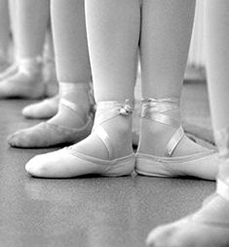 A black and white photo of a group of young girls wearing ballet shoes.