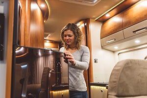 Woman in a motorhome, looking at a tablet, surrounded by wood cabinetry and seating.