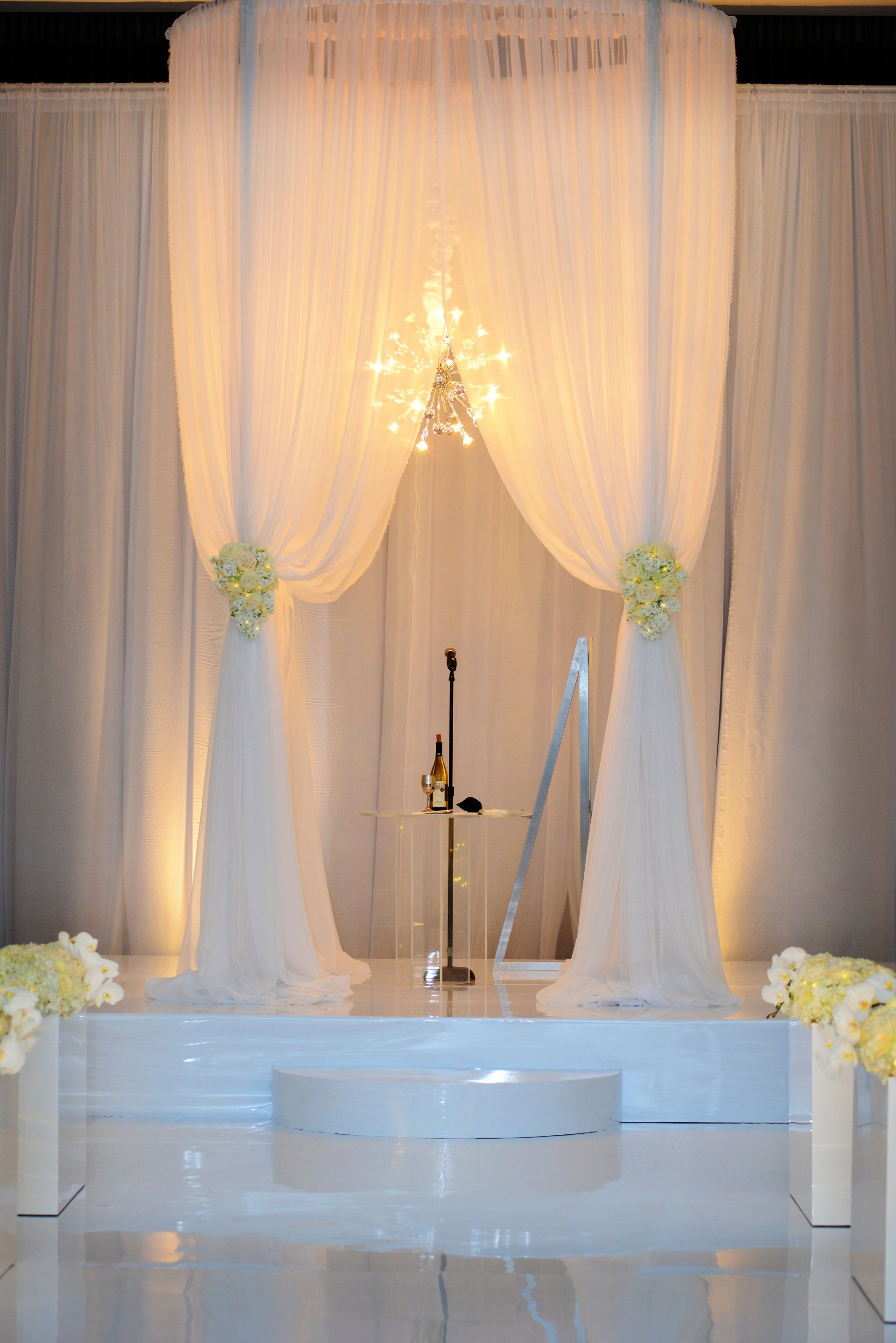 A white stage with a microphone and flowers in front of a white curtain.