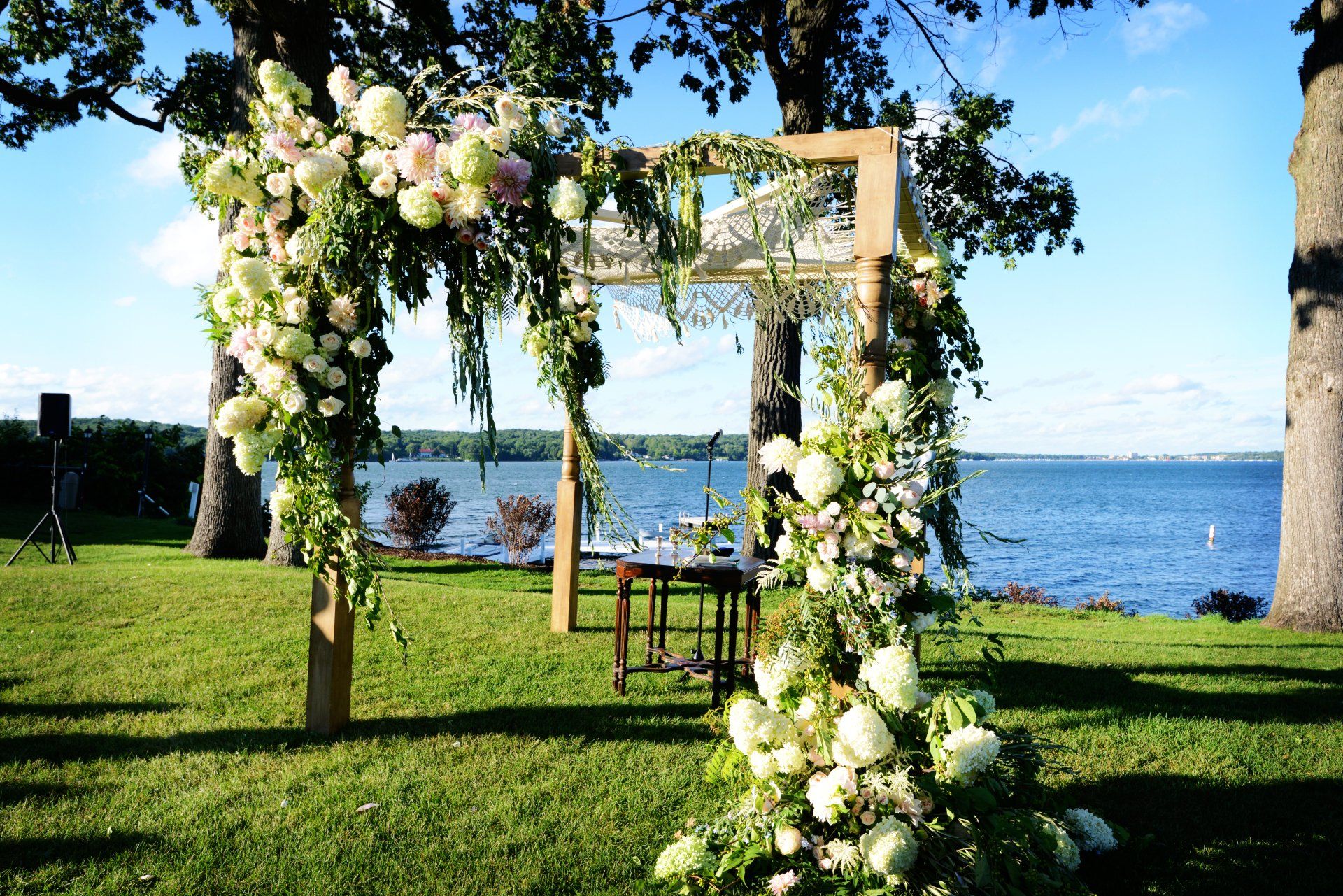 A wooden arch decorated with flowers and leaves in front of a body of water.