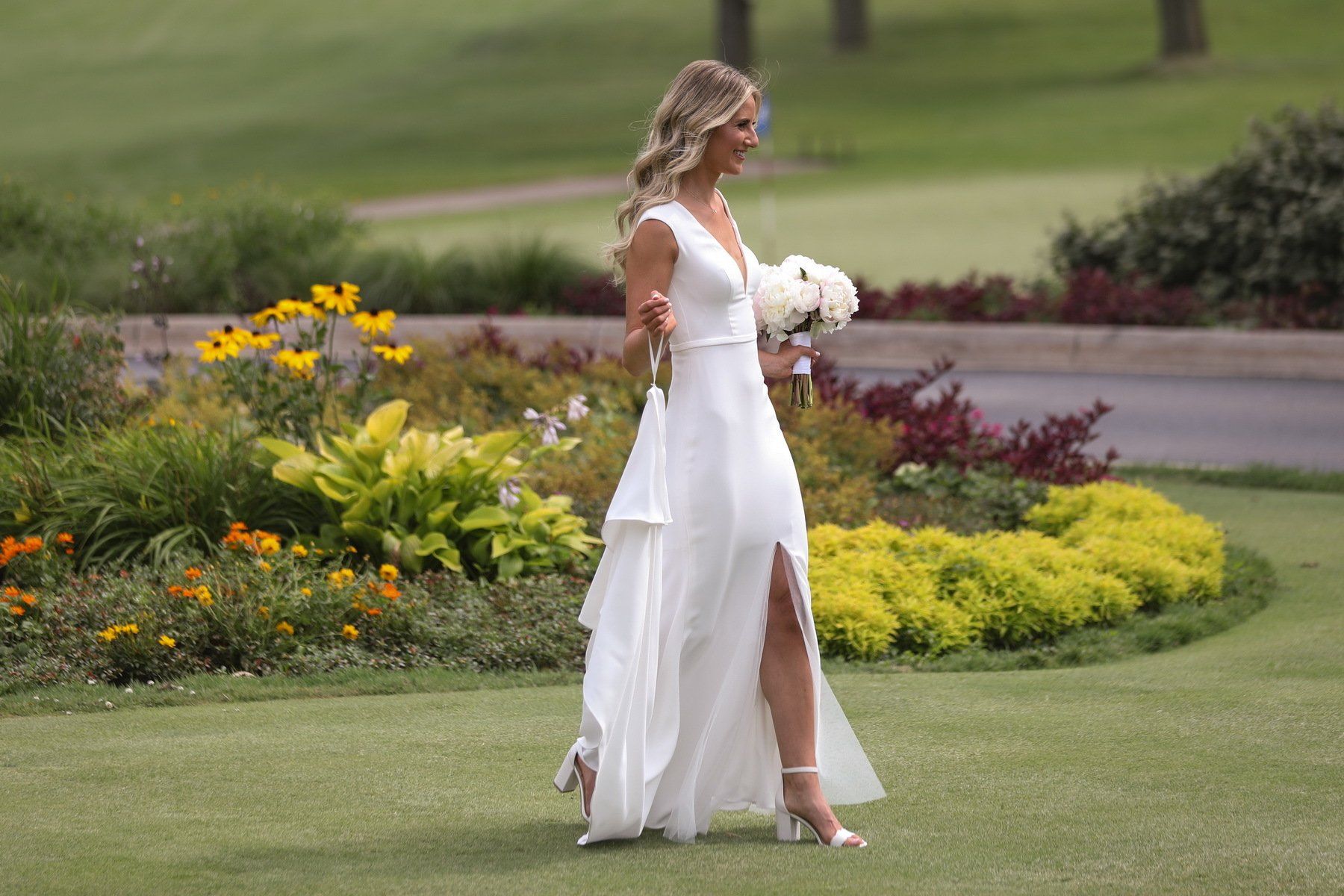 A bride in a white dress is walking down the aisle on a golf course.