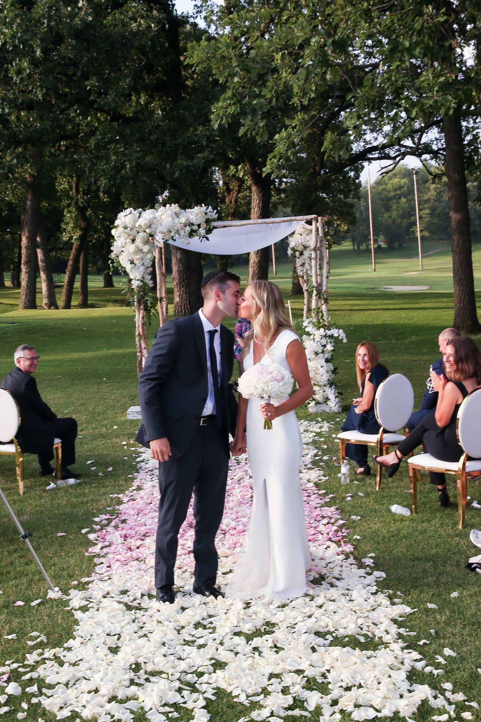 A bride and groom kissing at their wedding ceremony in a park.