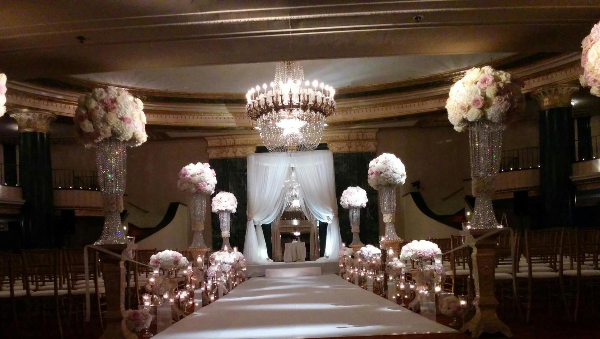 A wedding ceremony is taking place in a large room with flowers and candles.
