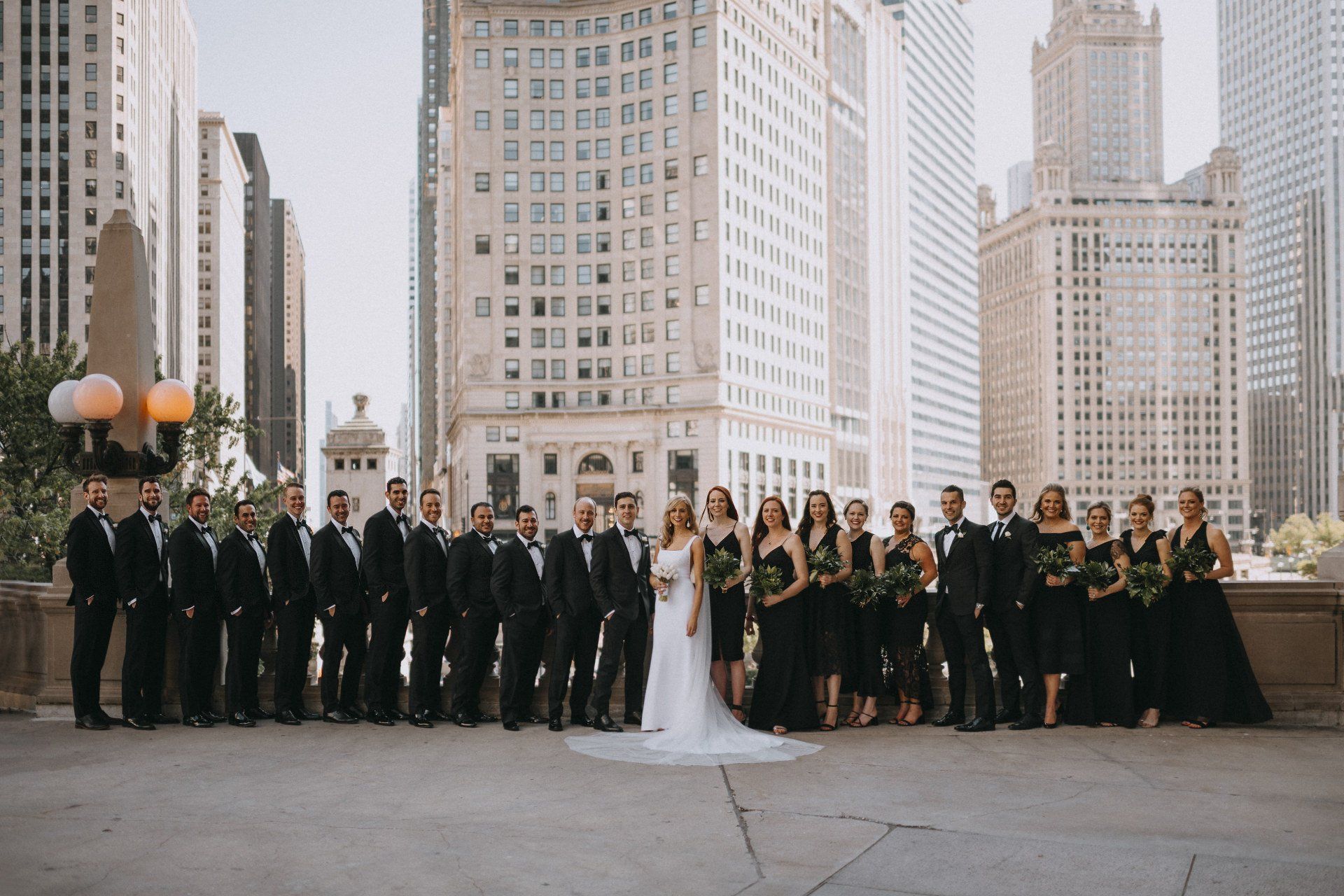A bride and groom are posing for a picture with their wedding party in front of a city skyline.