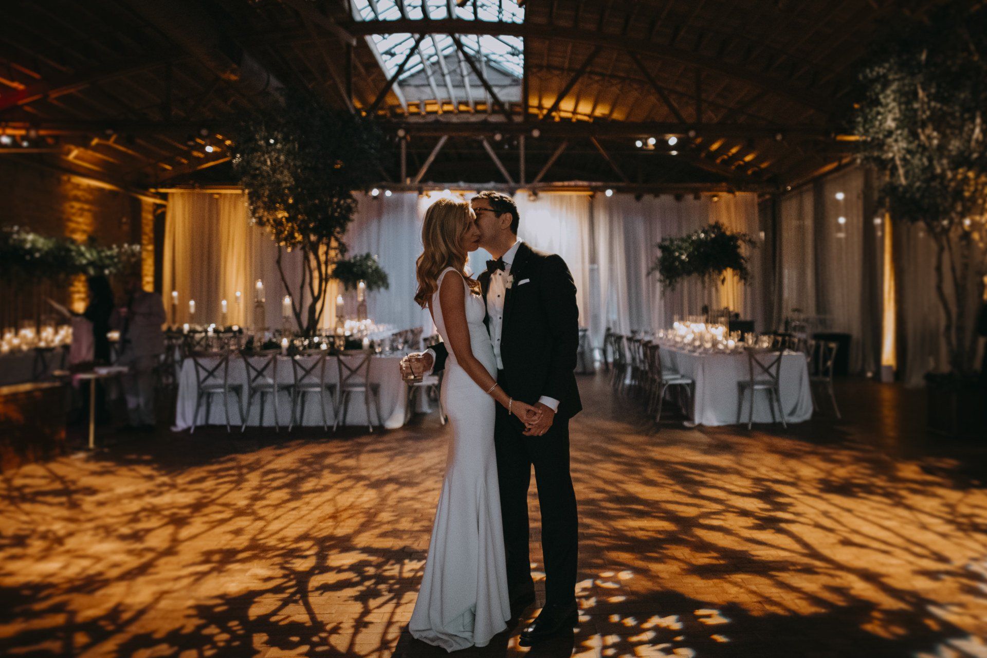 A bride and groom are kissing in a large room at their wedding reception.
