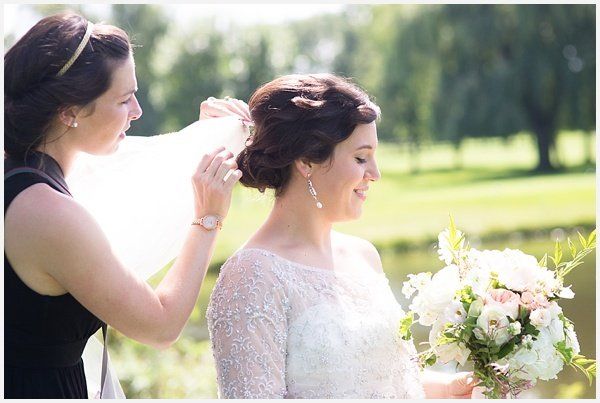 A woman is putting a veil on a bride 's head.