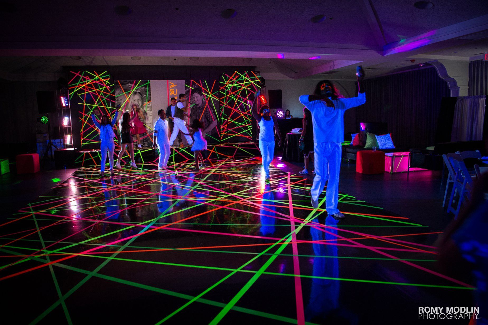 A group of people are dancing in a room with glow in the dark tape on the floor.