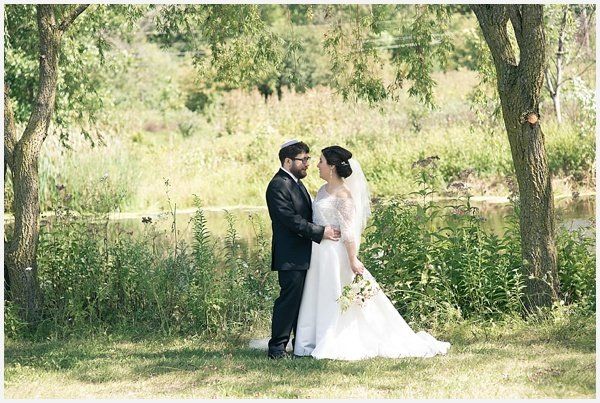 A bride and groom are standing in a field holding hands.