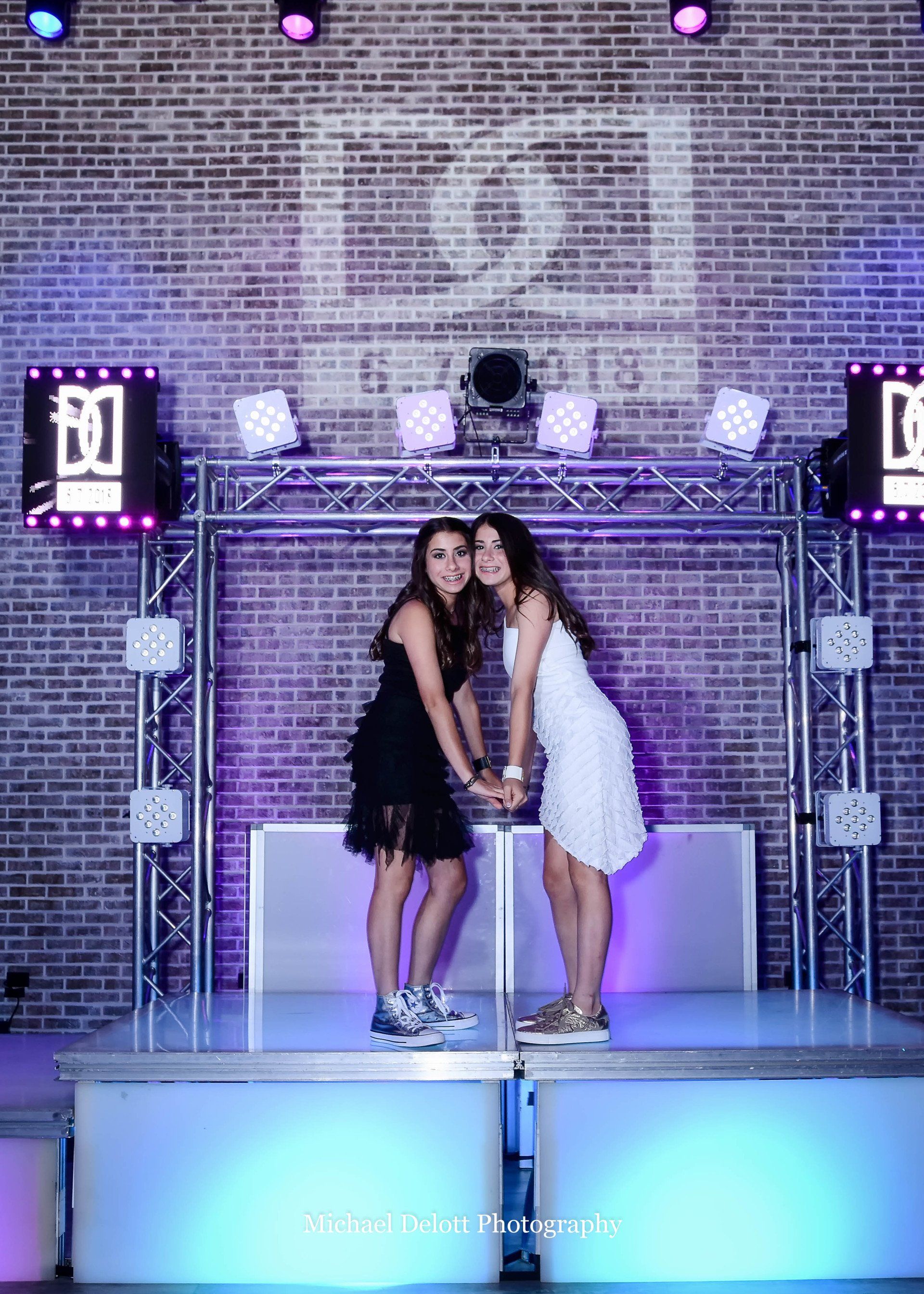 Two girls are standing next to each other on a stage in front of a brick wall.