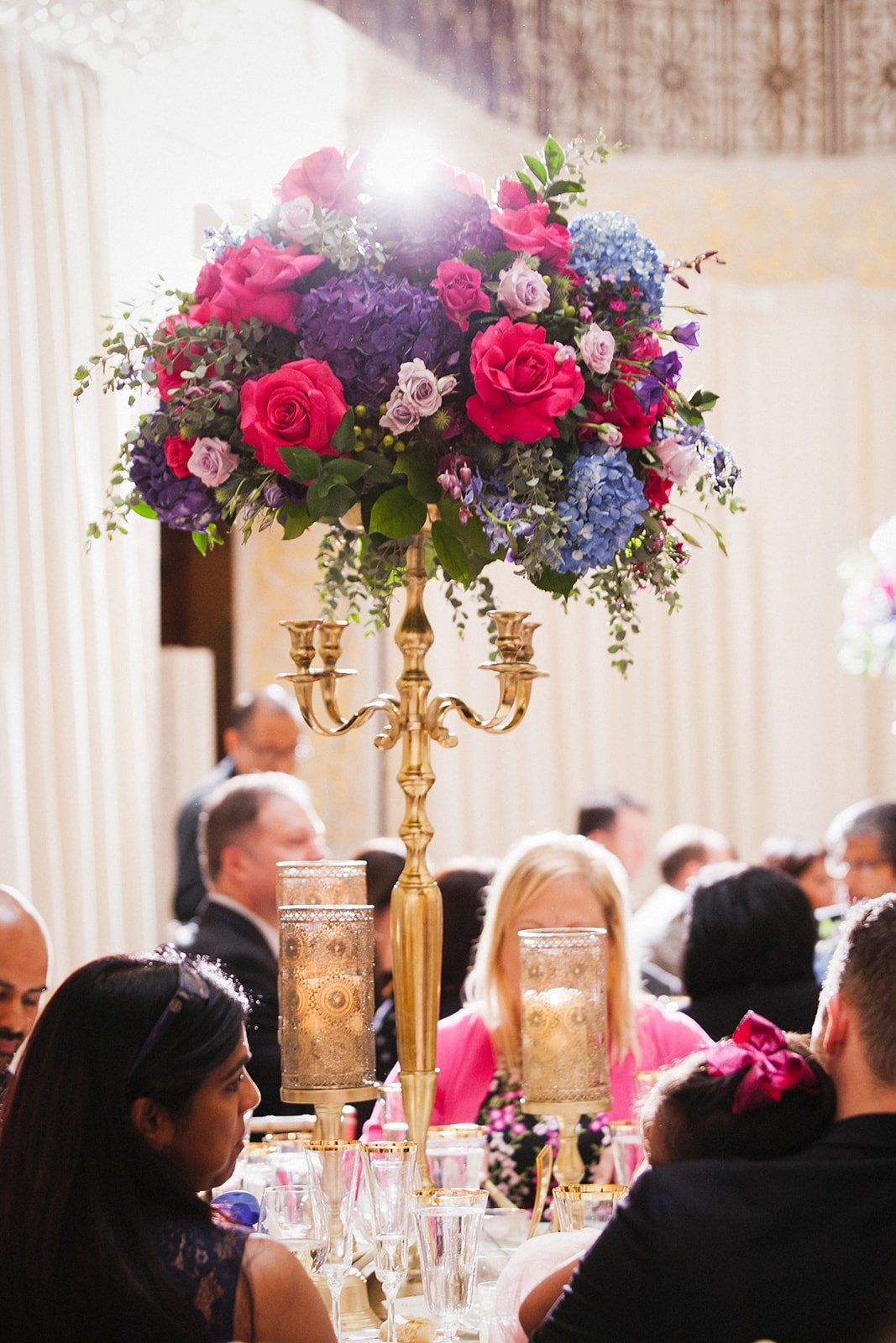 A group of people are sitting at a table with a candelabra filled with flowers.