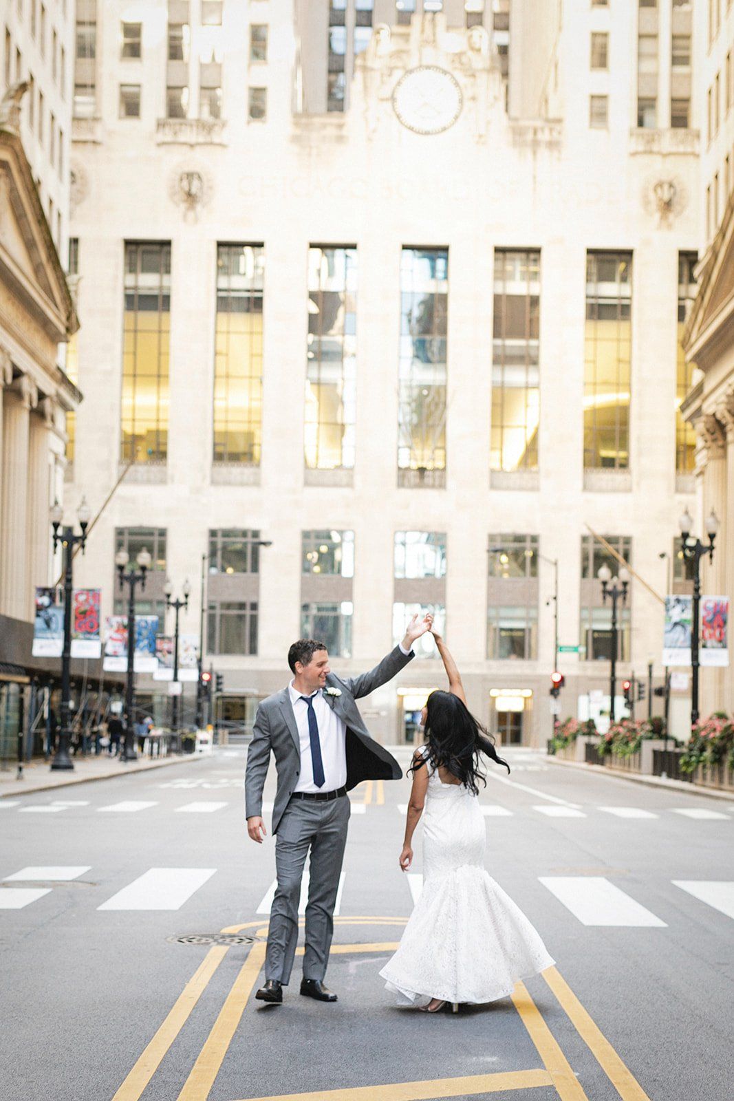 A bride and groom are dancing on the street in front of a building.