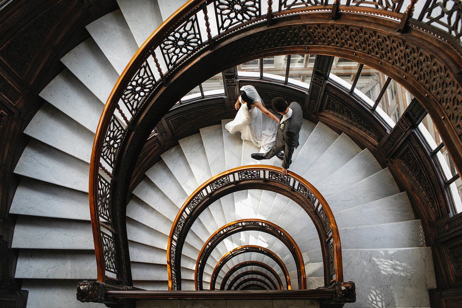 A bride and groom are walking down a spiral staircase.