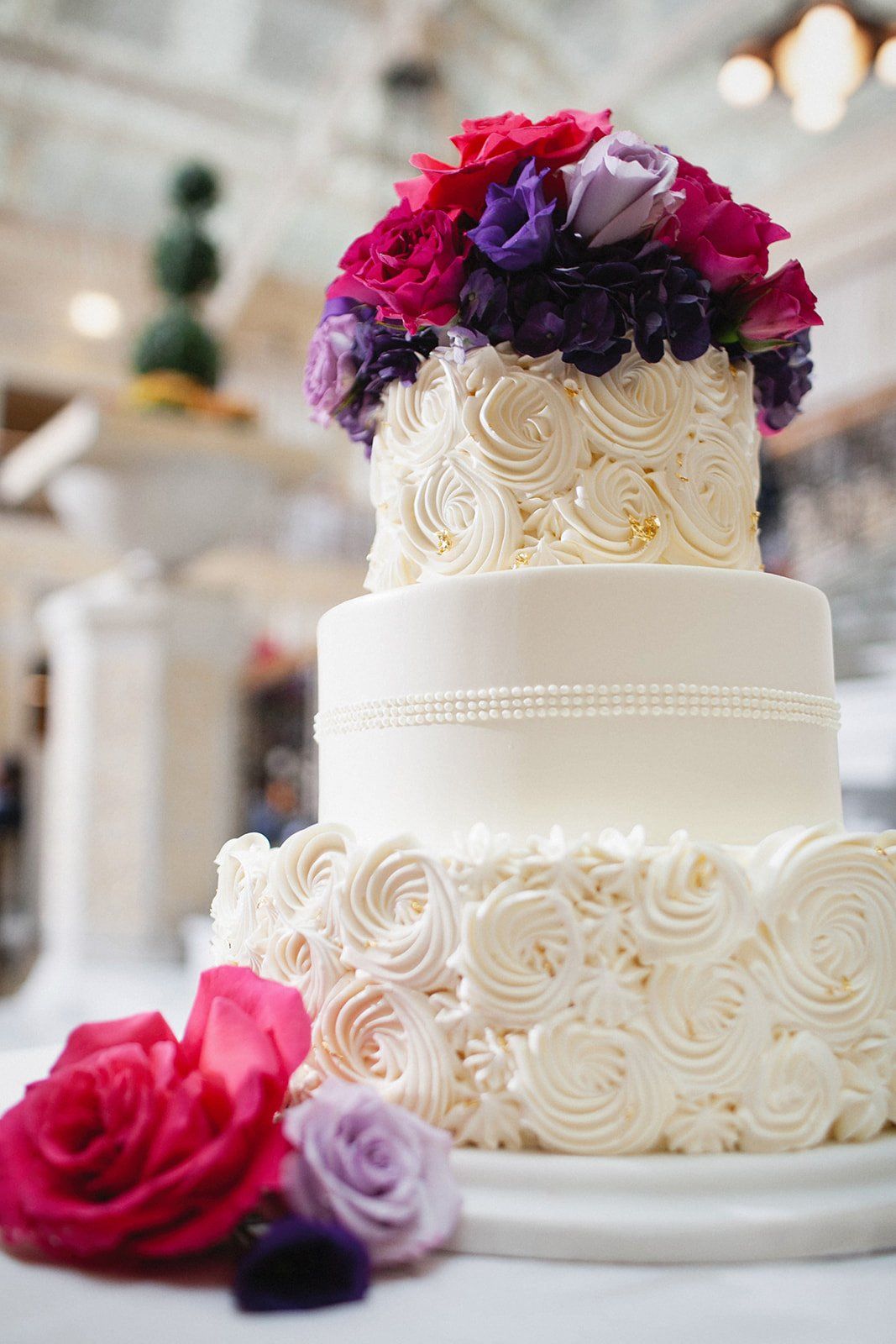 A white wedding cake with purple and pink flowers on top.