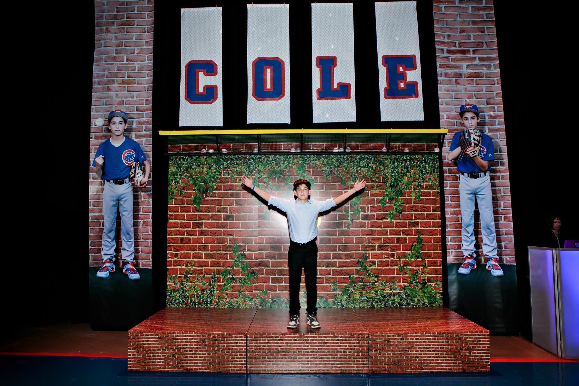 A boy is standing on a stage in front of a brick wall with the name cole on it.
